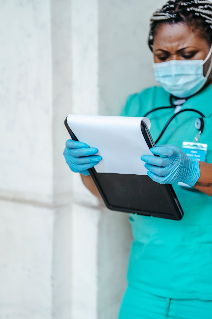 Crop African American female in uniform and gloves standing in hospital hallway and looking through papers